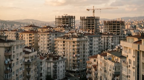 Gün batımı ışığında sık yerleşimli apartman blokları; çatılarda uydu antenleri, arkada vinçle yükselen iki inşaat hâlindeki bina